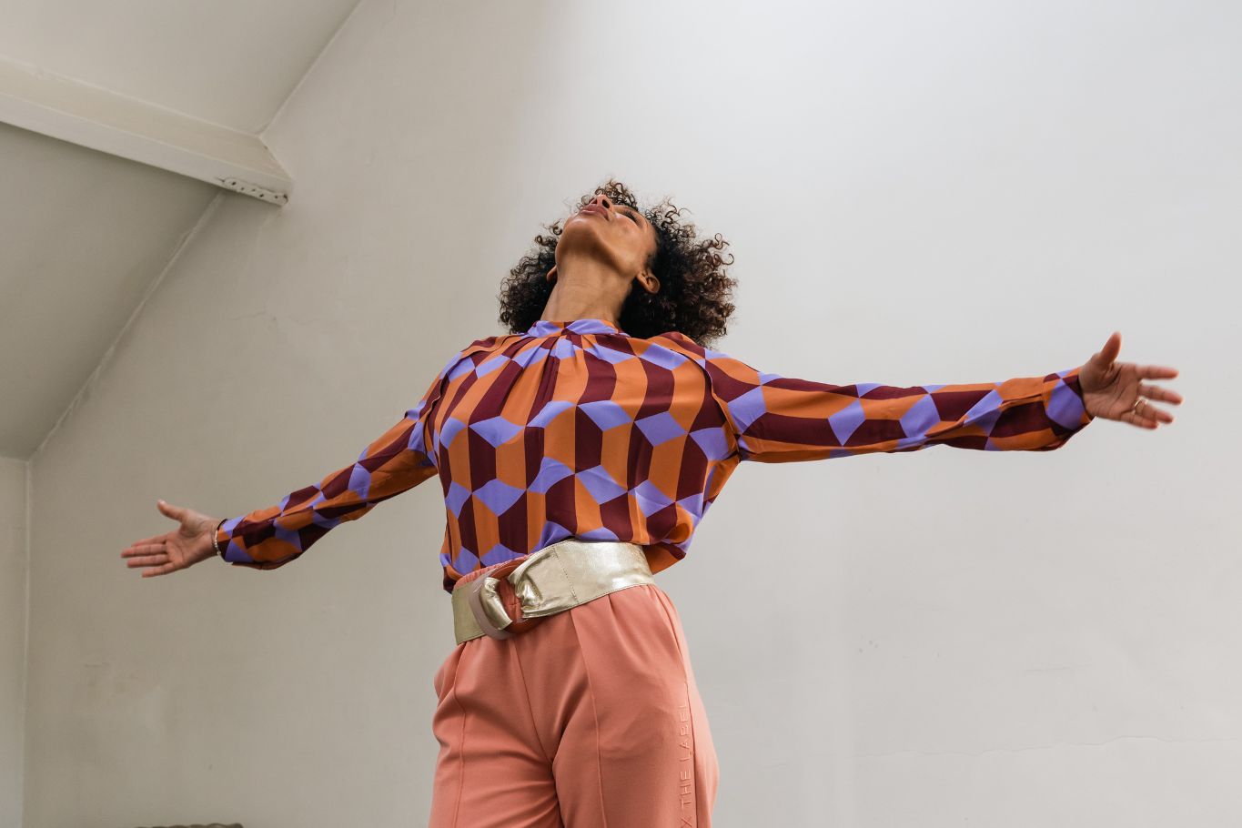 woman with arms open. She wears a purple-orange blouse with gold belt