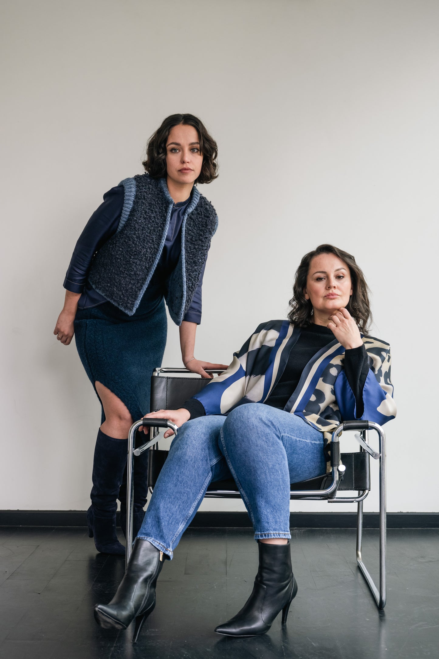 One woman in seat and wearing short silk kimono, other woman leaning on seat and wearing wool cardigan with wool skirt