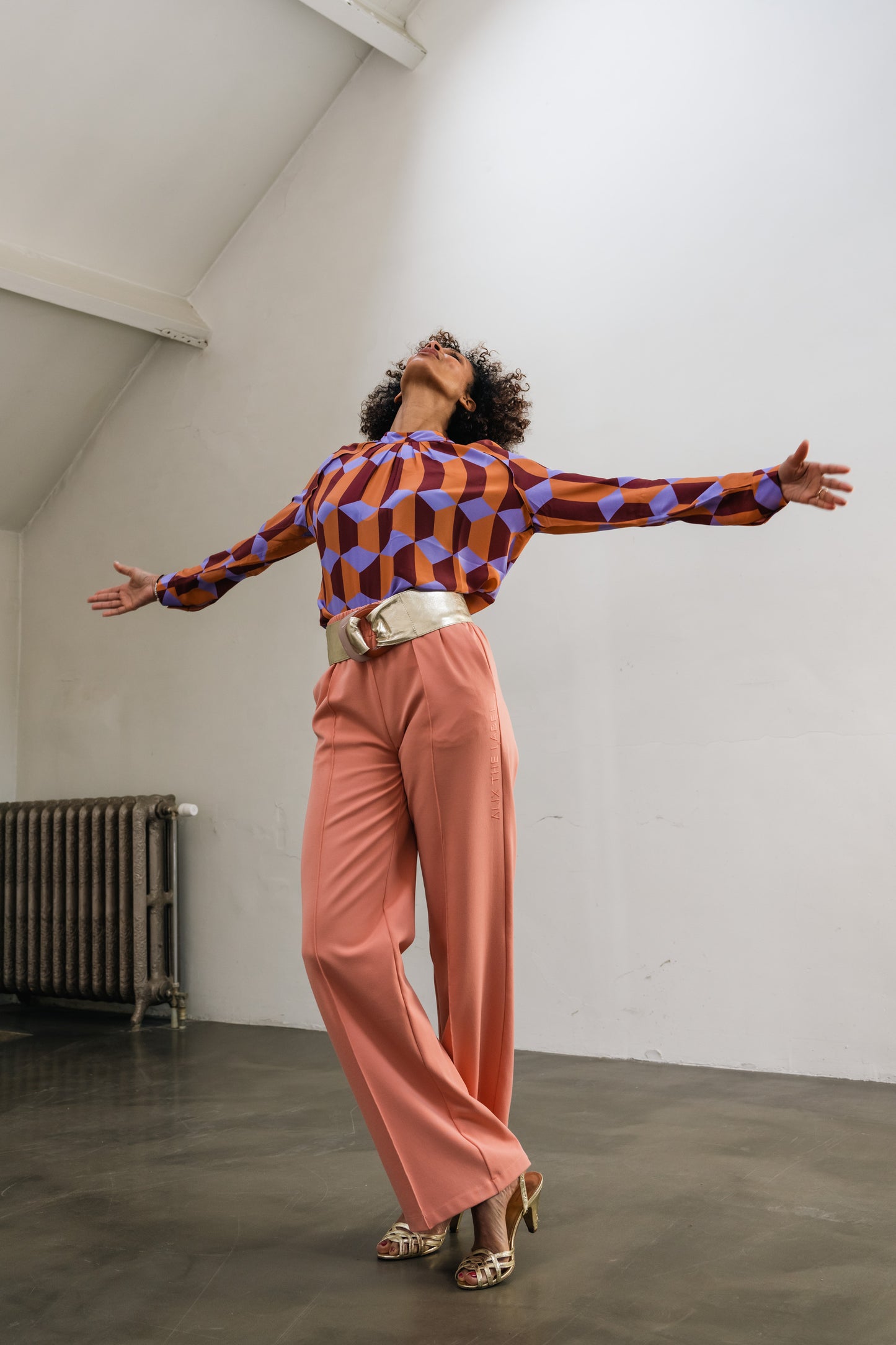 woman stretching arms open, wearing Orange-purple blouse with gold belt