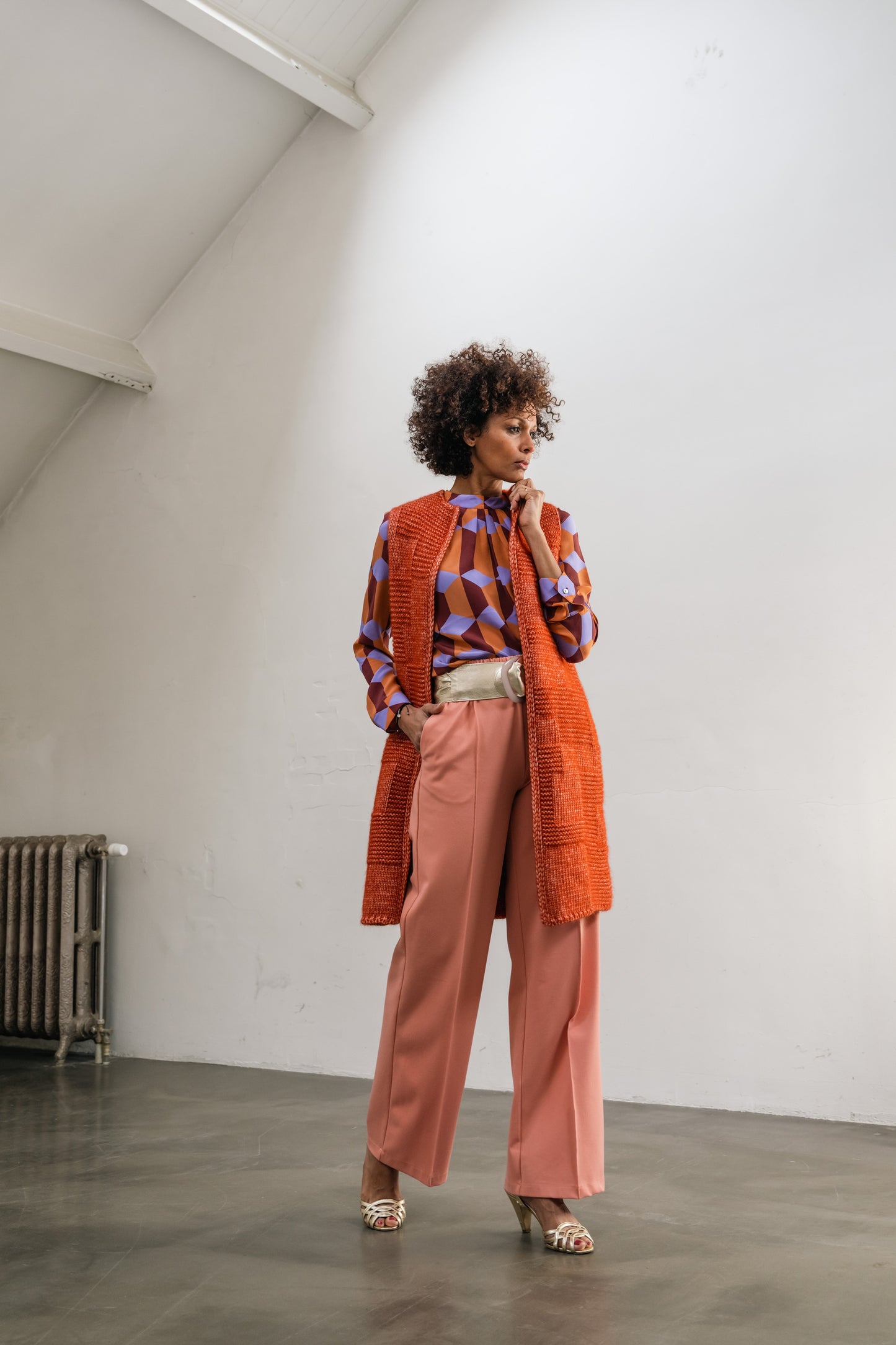 the woman wears an orange wool cardigan with silk blouse