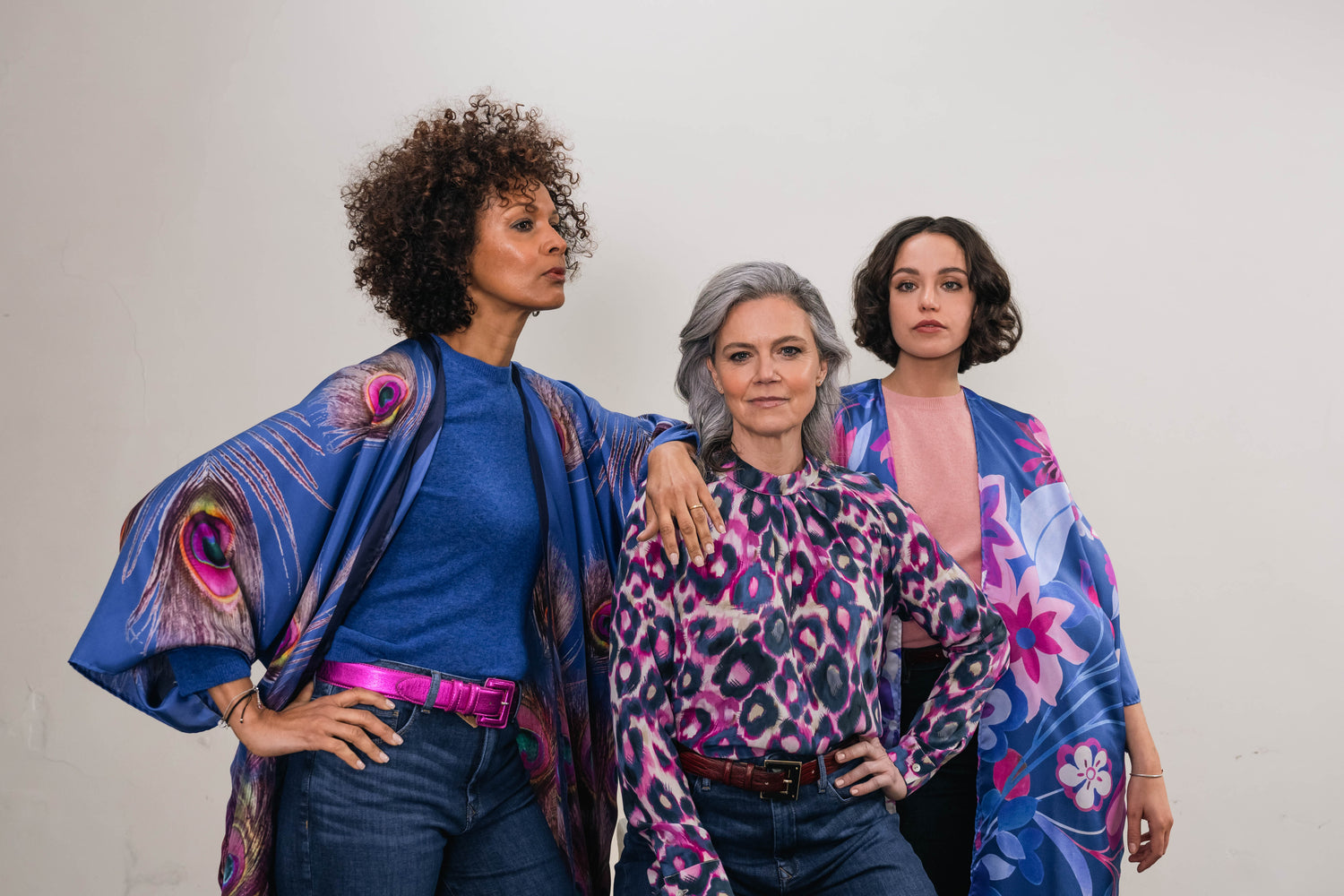 Three women all wearing garments in blue. Silk kimono with peacock feathers, blue blouse and a blue floral print kimono