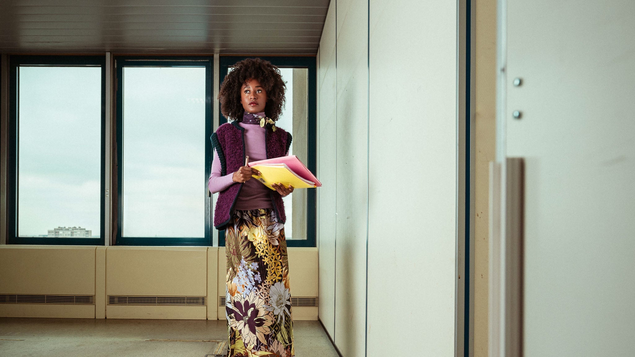 Woman wearing a purple knit vest over a lilac turtleneck, a floral maxi skirt, and a matching silk scarf in the same print 