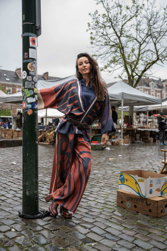 Girl leaning next to a pole, wearing a silk pants, blouse and kimono. On top of that, she wearing a bulky leather belt