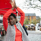 Black girl wearing a red sweater, a gray fluffy jacket, and a form-fitting gray skirt