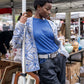 Black girl leaning against a tent, wearing a blue sweater with a special gray and blue jacquard pattern, a gray belt, and cool pants.