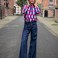 Women is wearing a wide jeans with small leather belt and blouse with unique print in fuchsia and dark blue