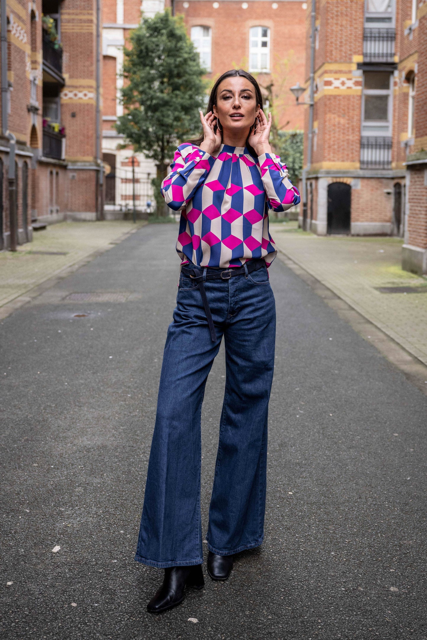 Women is wearing a wide jeans with small leather belt and blouse with unique print in fuchsia and dark blue