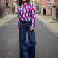 women is wearing unique blouse in geographic print with dark blue and fuschia colours. Jeans with belt underneath