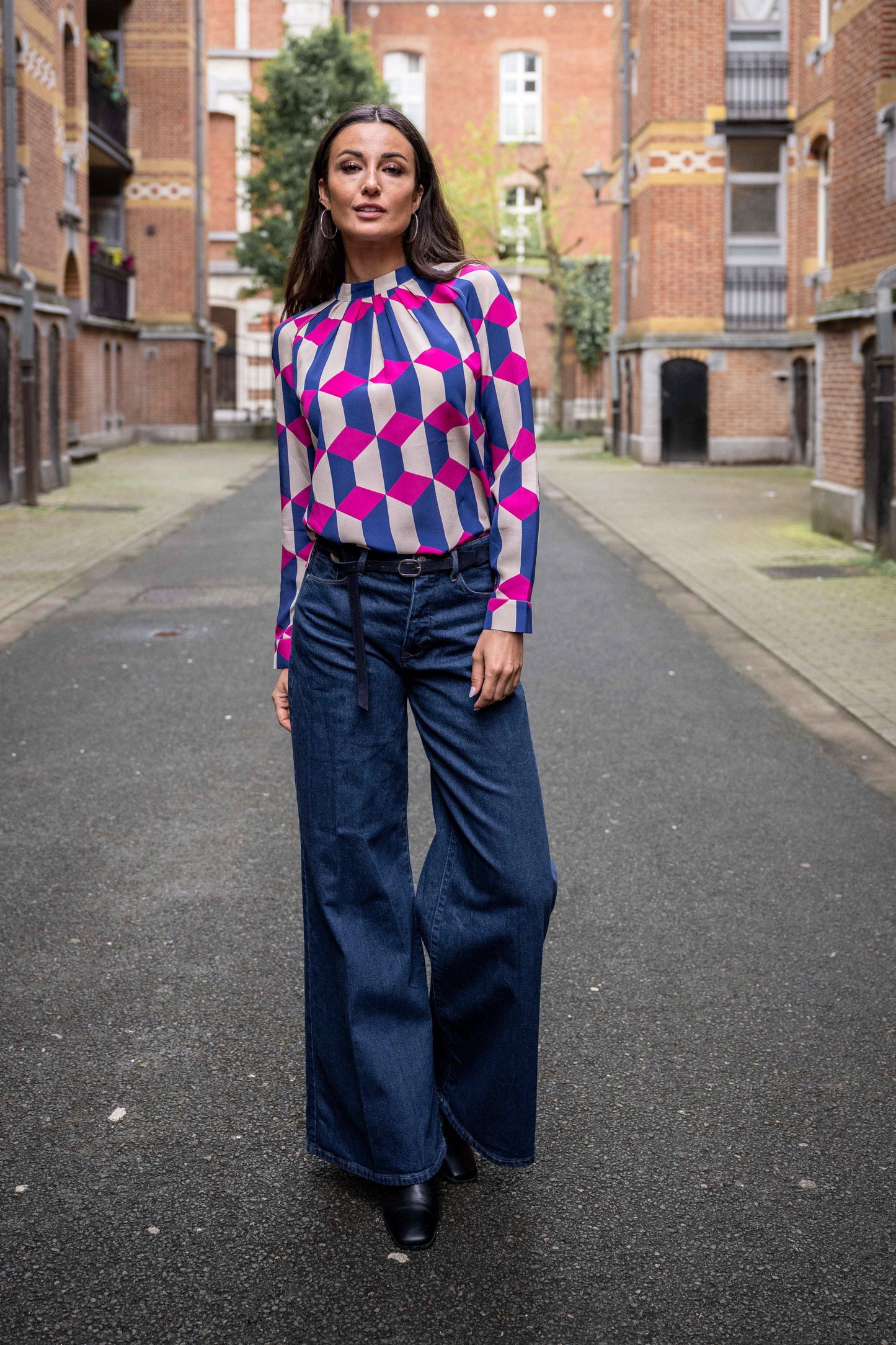 women is wearing unique blouse in geographic print with dark blue and fuschia colours. Jeans with belt underneath