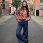 girl wearing a dark blue beanie, silk blouse with leopard print, jeans, cowboy boots and a leather belt