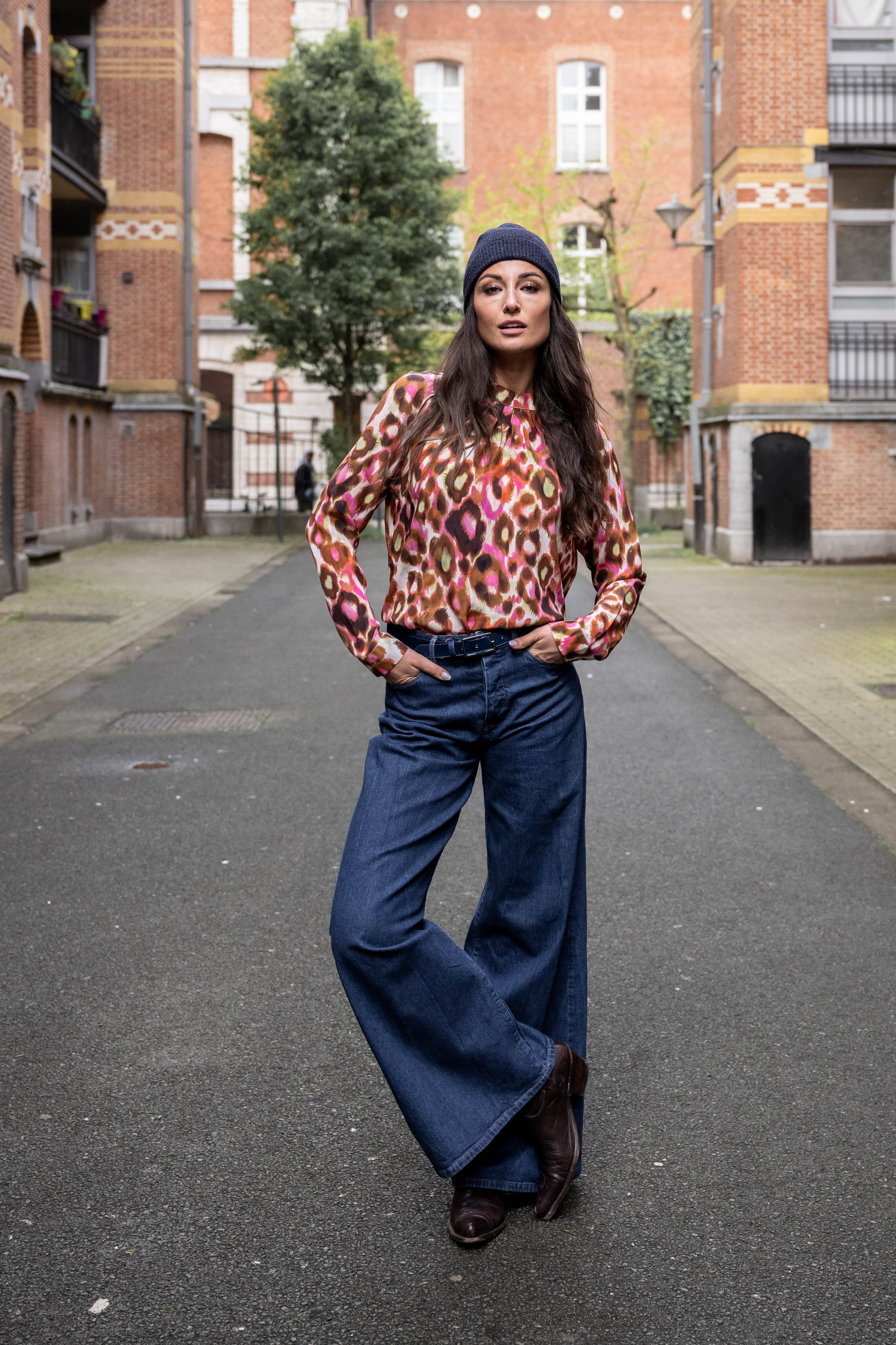 girl wearing a dark blue beanie, silk blouse with leopard print, jeans, cowboy boots and a leather belt