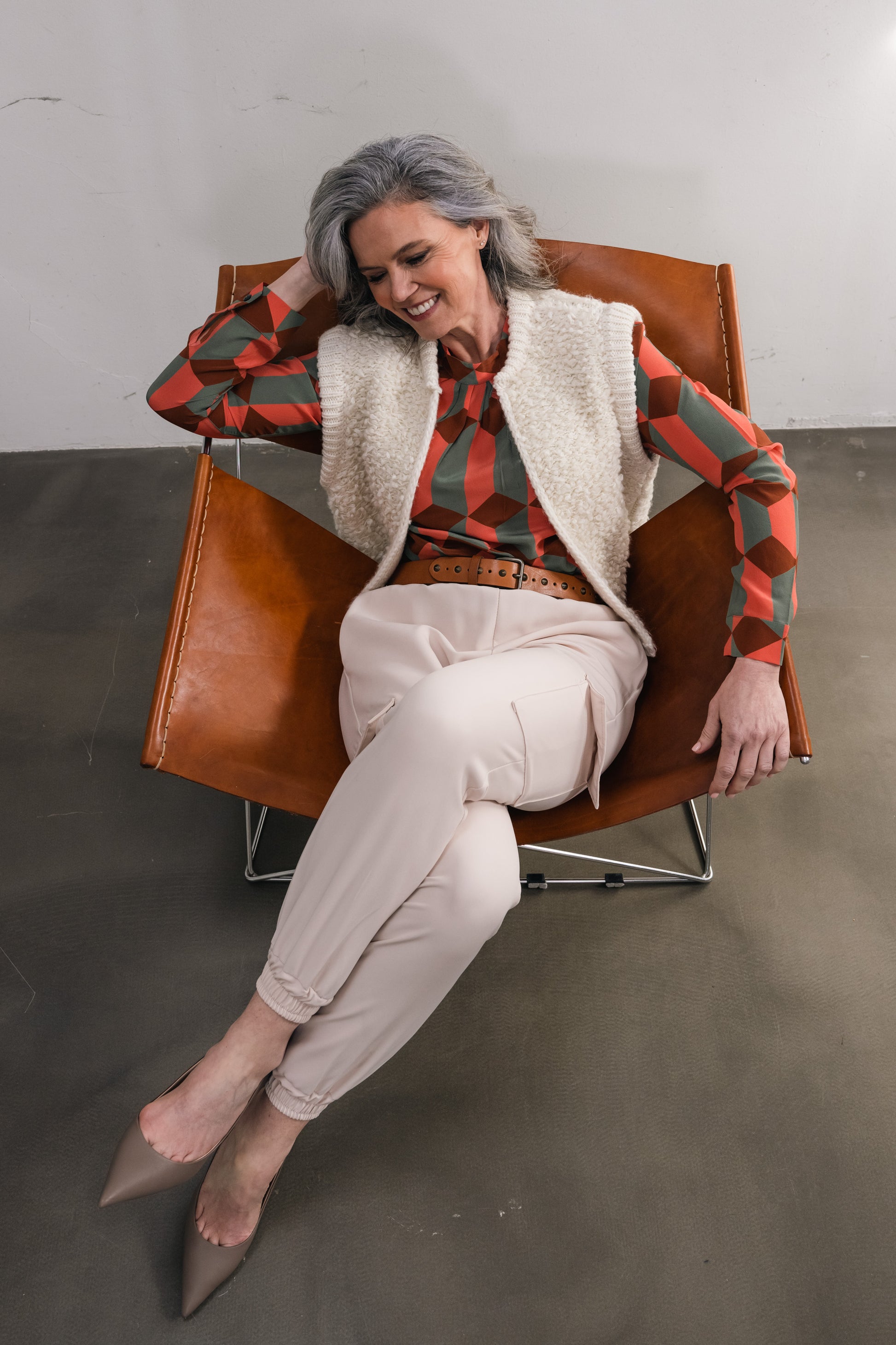 elderly woman sitting in a chair wearing a silk blouse in shades of orange-green and a white wool cardigan