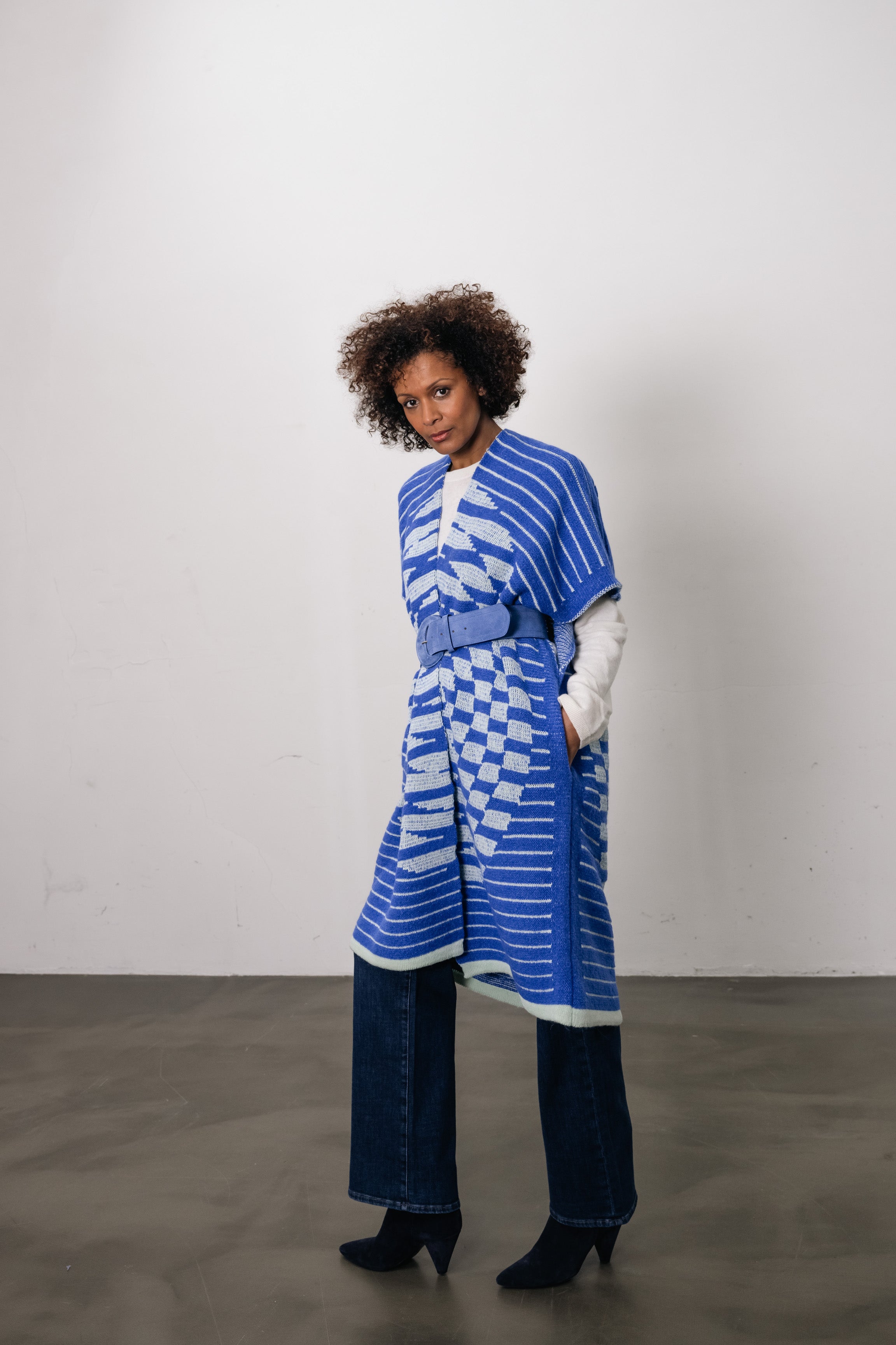 woman wears blue vest with circle on back. On top of the blue vest, she wears a wide blue belt