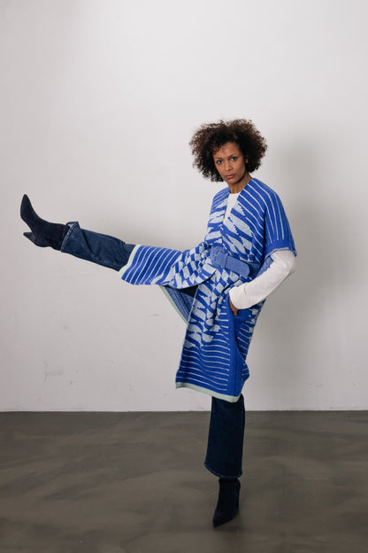 woman wears blue vest with circle on back and puts her leg up in the air. On top of the blue vest, she wears a wide blue belt