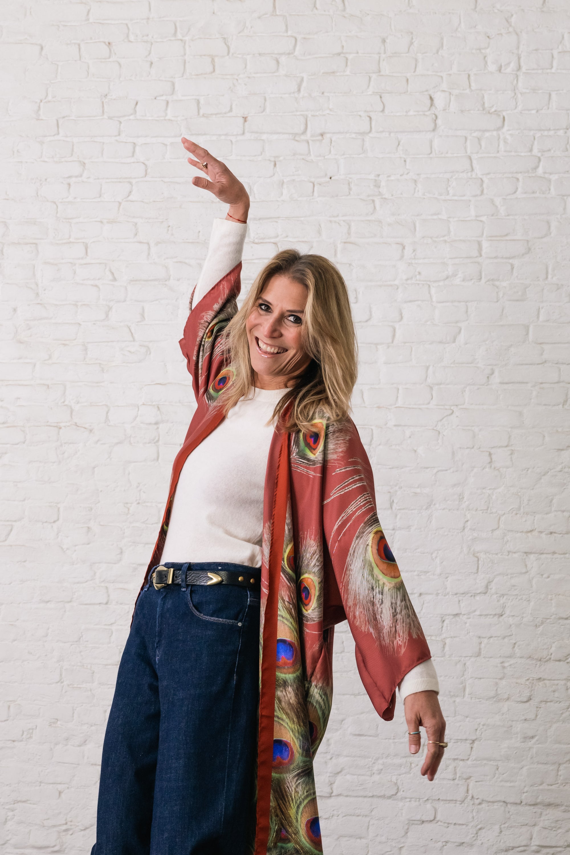 woman raising her hands in the air, wearing a cowboy belt and silk kimono in bordeaux with peacock feathers