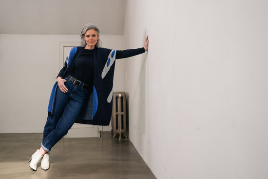 lady wearing dark blue wool cardigan leans against a wall