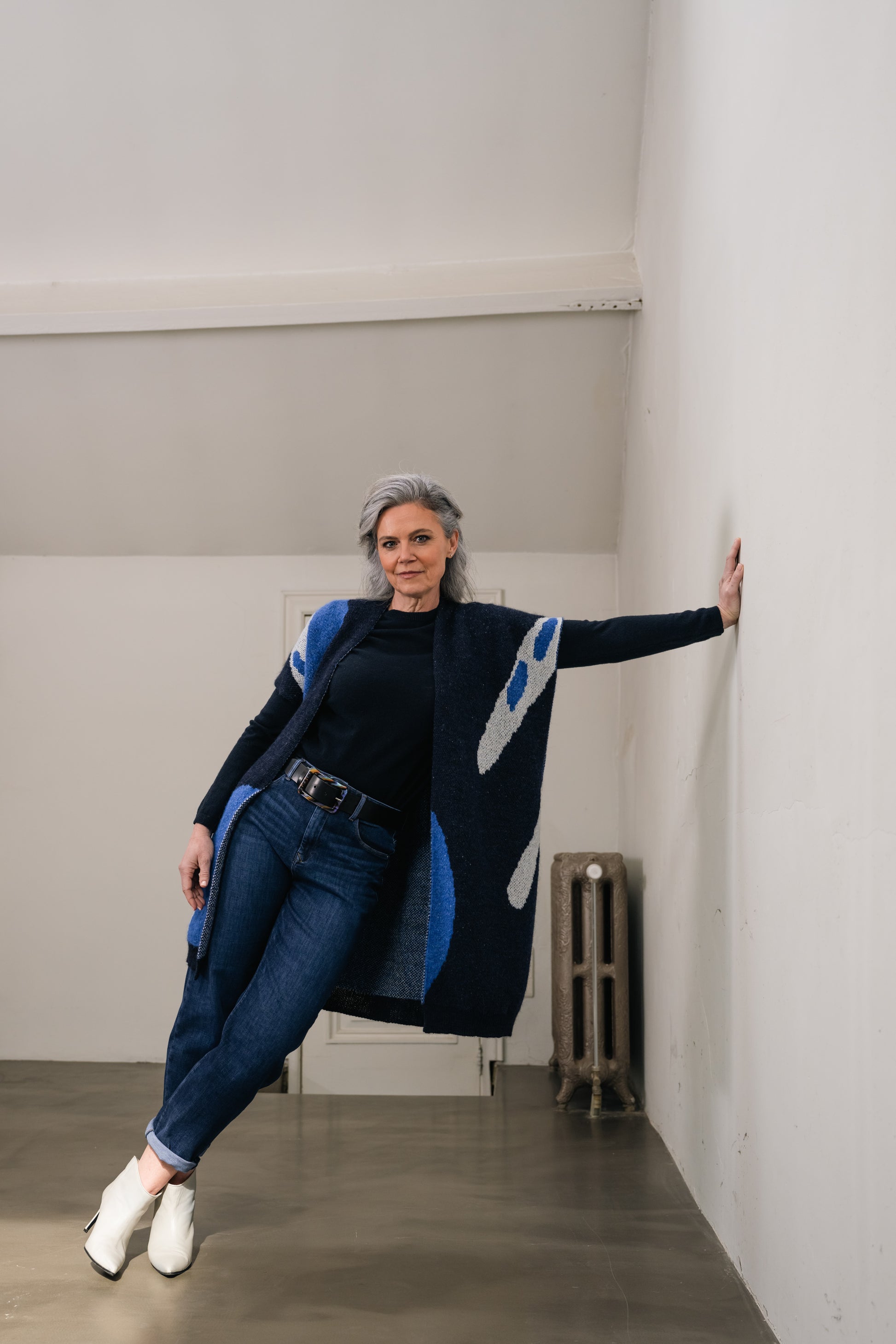 woman stands with her hand against the wall and wears a blue wool cardigan with print